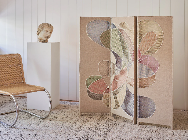 Decorative room divider with abstract multicoloured fabric design, next to a sculptural bust and woven chair